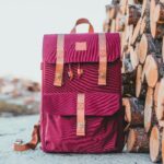 Pink backpack with leather straps next to stacked firewood, showcasing outdoor adventure gear.